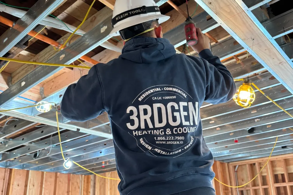 3rdGen commercial mechanical technician installing overhead ductwork and piping at a Bay Area construction site
