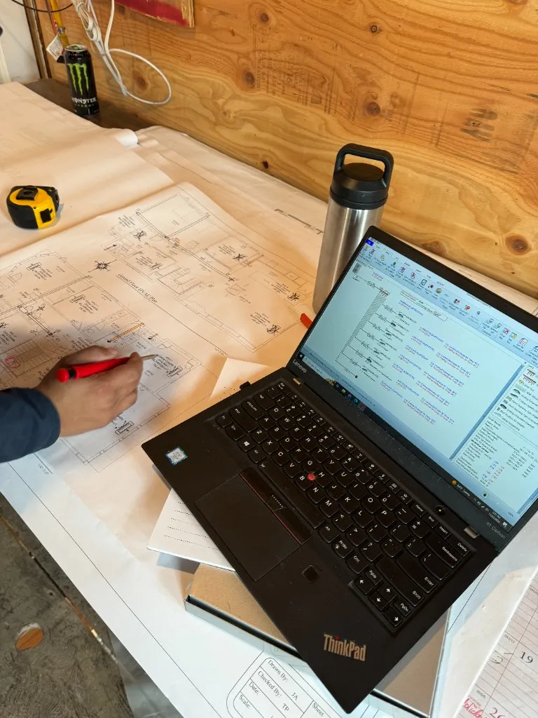 Reviewing a ground-floor HVAC plan next to load calculation data on a job-site workbench